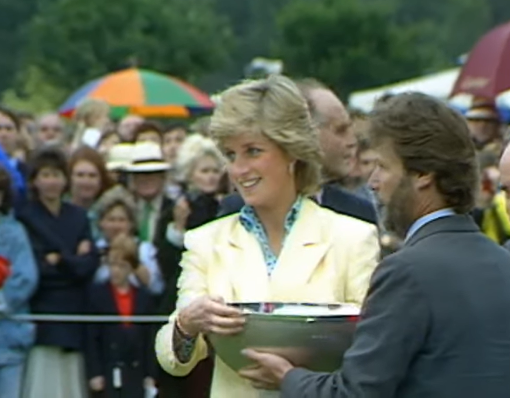 Princess Diana gaining an award from a person in a gray suit, the audience behind her